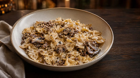 Wide view of creamy bowtie pasta with ground beef, sautéed mushrooms and minced black truffle in a ceramic bowl.