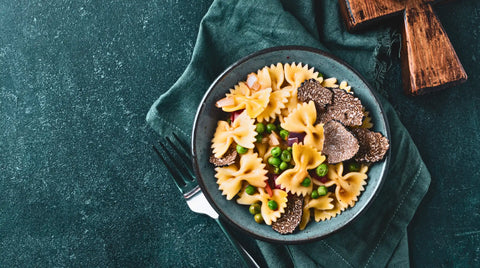 A bowl of bow-tie pasta with peas and sliced black truffles