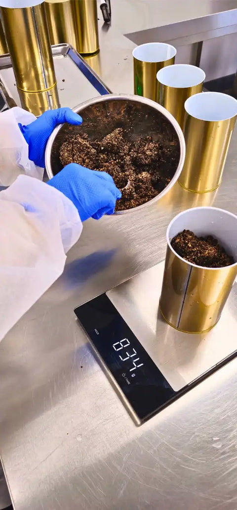 Gold-colored cylindrical containers being filled with dark, crumbly material.